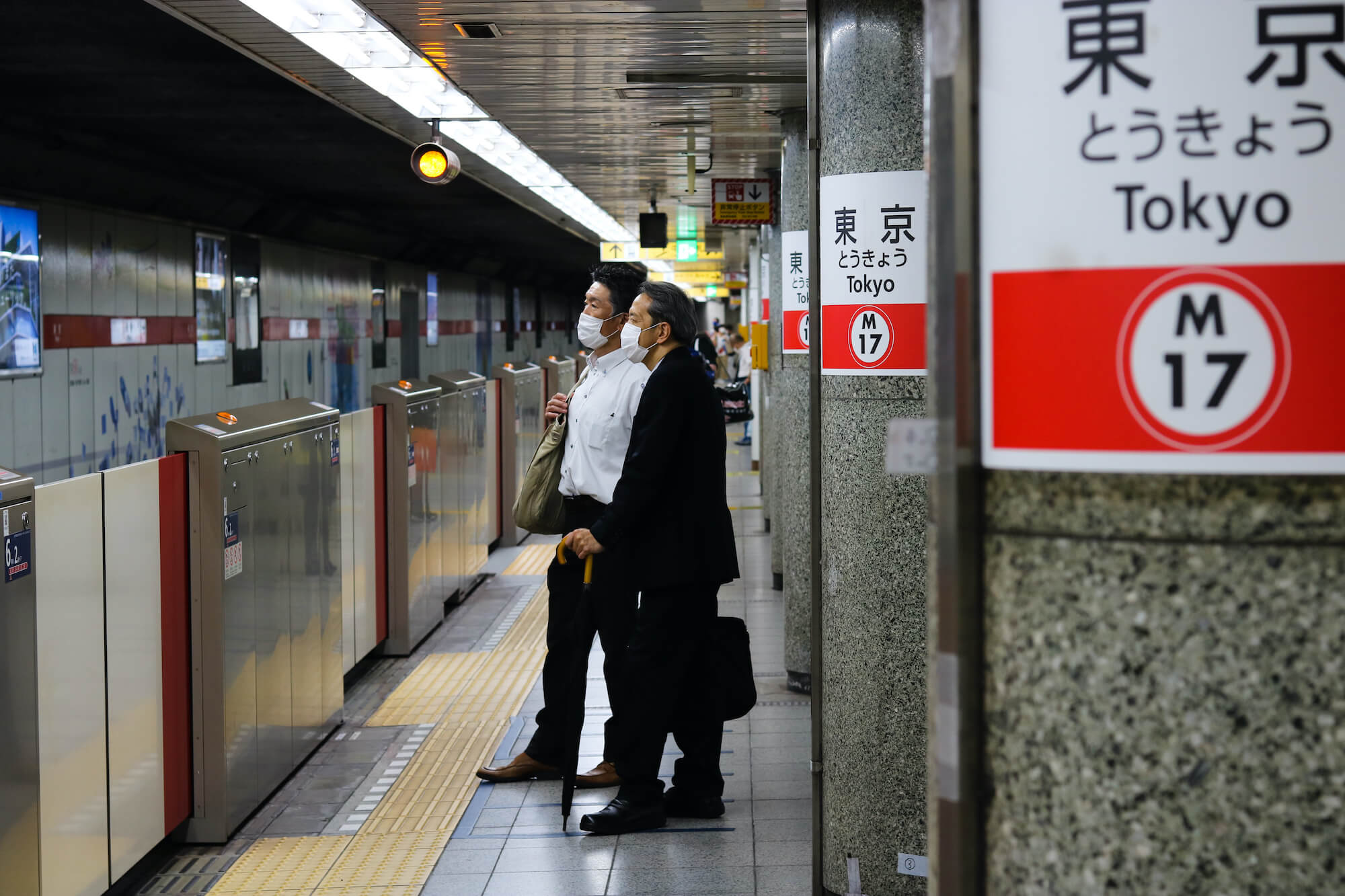 Maskierte Männer warten in Tokio auf ihre Bahn.