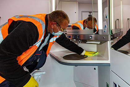 DB Mitarbeiter reinigt Waschbecken auf Bordtoilette.