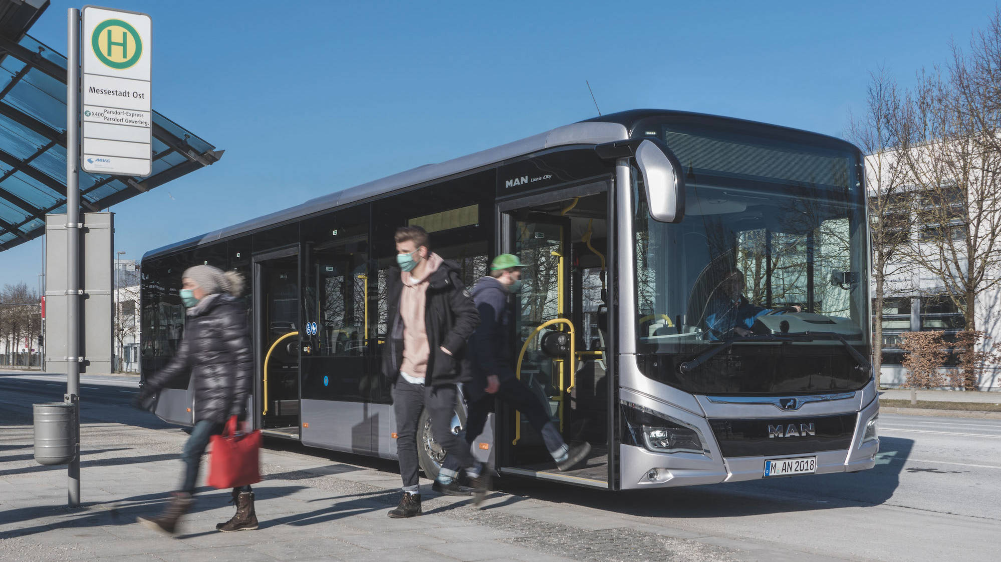 Menschen mit Masken steigen an einer Haltestelle aus einem Bus