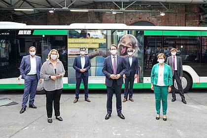 Akteure der Verkehrsbranche posieren vor einem #BesserWeiter-Kampagnenbus.