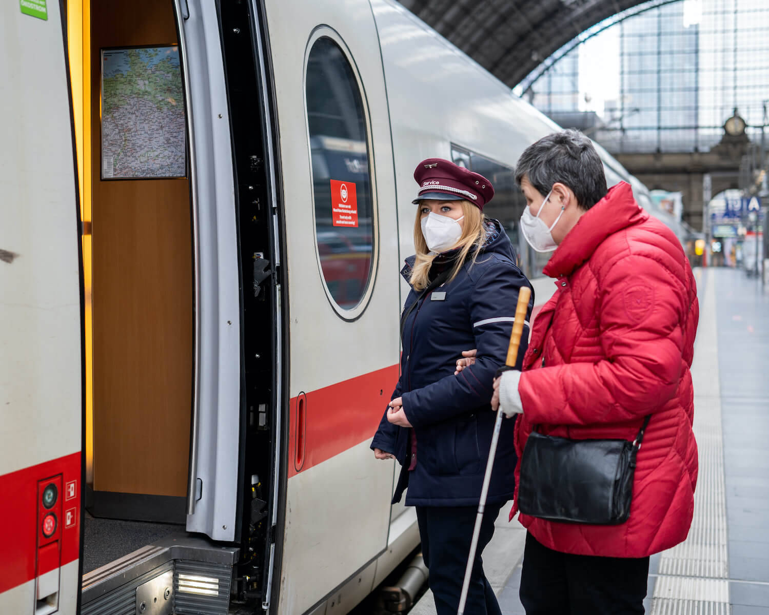 Eine DB-Mitarbeiterin mit FFP2-Maske begleitet eine Frau mit eingeschränkter Sehfähigkeit in einen ICE