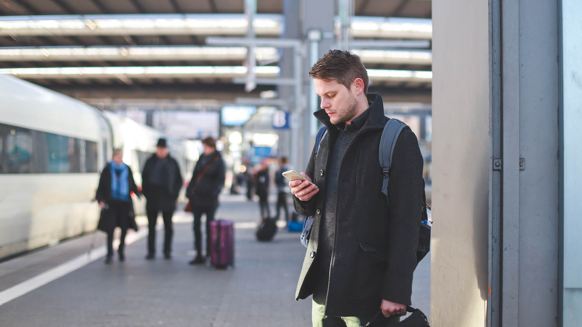 Mann schaut am Bahngleis auf sein Handy