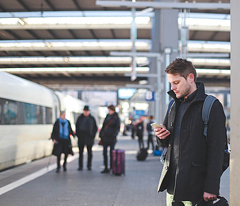 Mann schaut am Bahngleis auf sein Handy