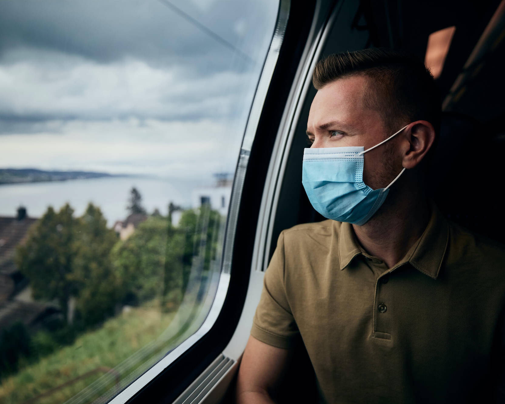 Mann sitzt mit Maske im Zug und schaut aus dem Fenster.