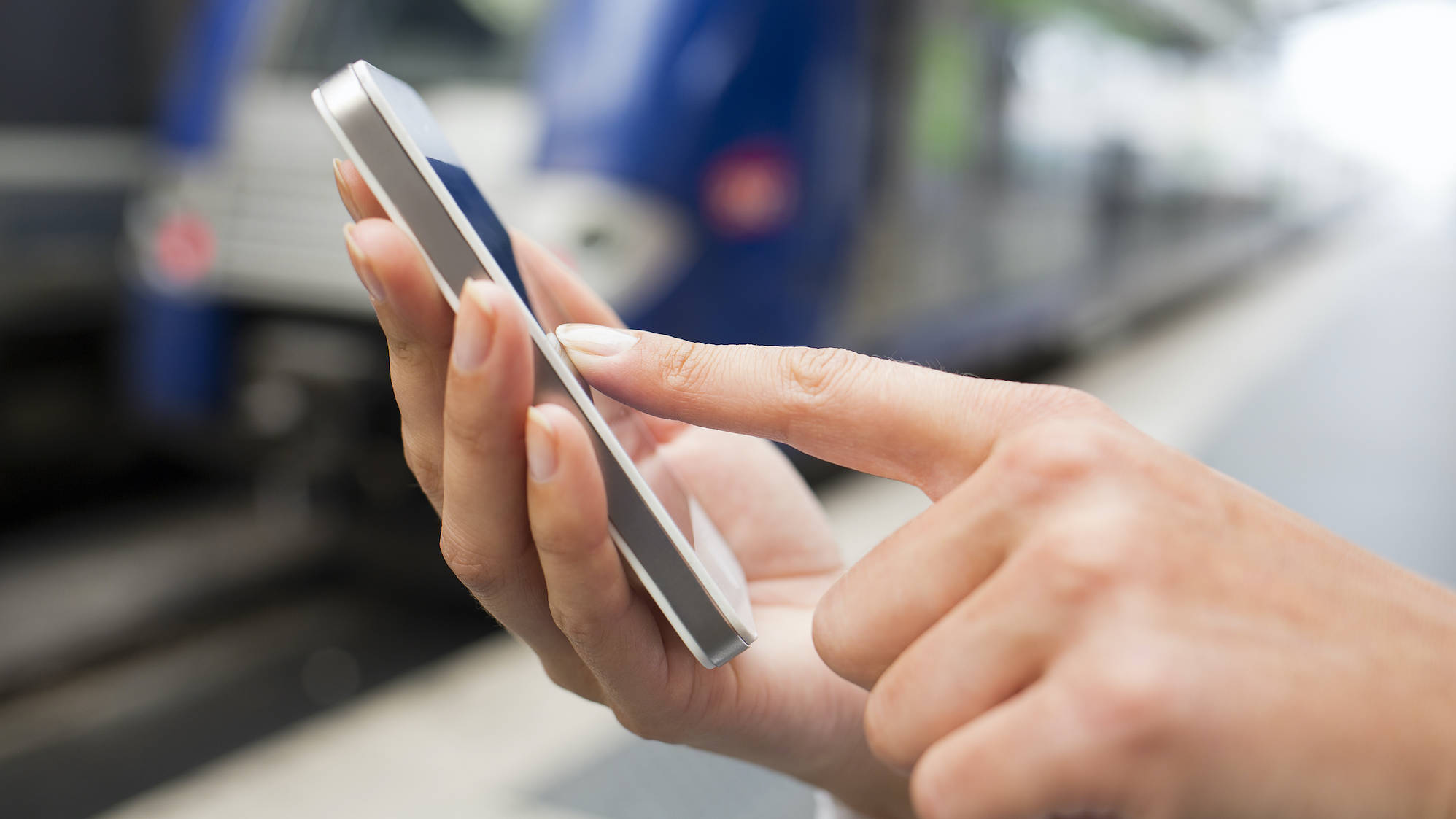 Frau bedient ihr Smartphone am Bahngleis