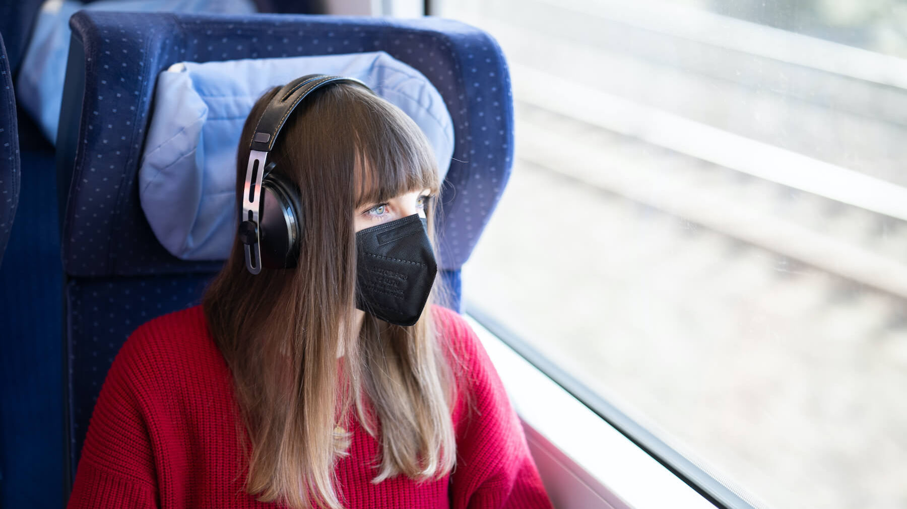 Frau sitzt mit Maske in der Bahn und hört Musik