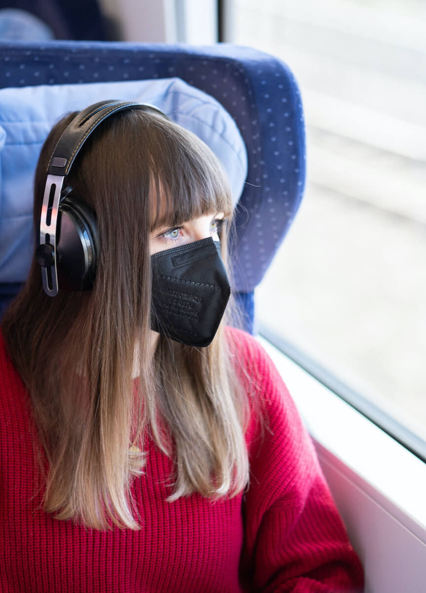 Frau sitzt mit Maske in der Bahn und hört Musik