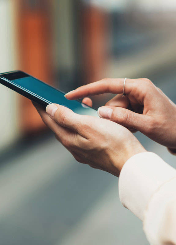 Frau steht mit ihrem Smartphone vor der Bahn.